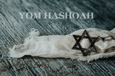 Yazı Yom Hashoah ve eski ve paslı bir kolye, gri, ahşap bir yüzeye yerleştirilmiş paçavra bir bez parçasının üzerinde Davut yıldızı şeklinde.