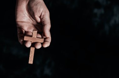 Adam elinde ahşap bir haç tutuyor, sağında boş bir alan olan siyah noktalı bir zemin üzerinde.