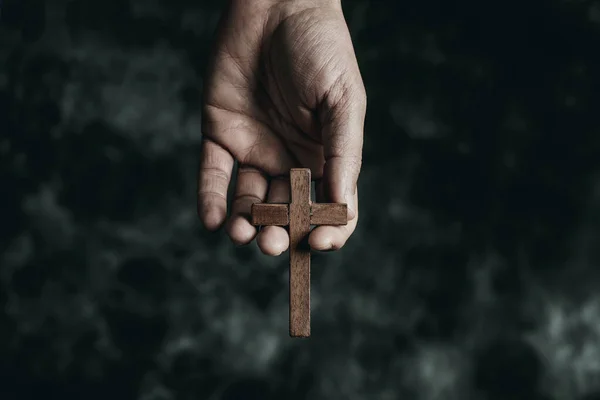 一个男人手里拿着一个木制的十字架 背景是黑黑的斑驳的 — 图库照片