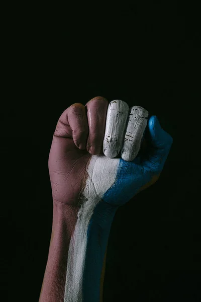 the clenched fist of a person with the transgender pride flag painted in it, on a black background, with some blank space on top