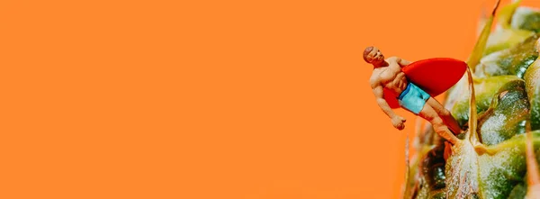 Miniaturní Muž Plavkách Červeným Surfovacím Prknem Ananasu Oranžovém Pozadí Panoramatickém — Stock fotografie