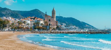 Sitges, Spain - March 3, 2022: A view of the Platja de la Fragata beach in Sitges, Spain, highlighting the Sant Bartomeu i Santa Tecla Church in the centre in a higher position