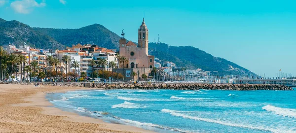 Sitges, İspanya - 3 Mart 2022: İspanya 'nın Sitges kentindeki Platja de la Fragata plajının manzarası, merkezde yer alan Sant Bartomeu i Santa Tecla Kilisesi' ni vurguluyor.