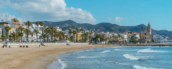 Sitges, İspanya - 3 Mart 2022: Arka planda Platja de la Fragata plajı ve Sant Bartomeu i Santa Tecla Kilisesi ile İspanya 'nın panoramik manzarası