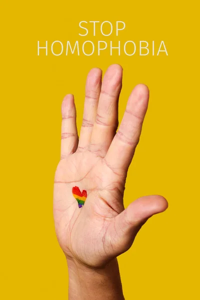 テキストは彼の手のひらに描かれたハート型の虹の旗を持つ男の同性愛嫌悪と上げ手を 黄色の背景に停止します — ストック写真