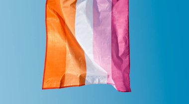 Lezbiyen gurur bayrağının yakın çekimi, arkadan görülüyor, güneşli bir günde rüzgarda gökyüzüne karşı sallanıyor.