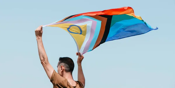 一名男子头顶上方的天空摇曳着一面双性包容的进步骄傲旗 以全景形式作为网页横幅 — 图库照片