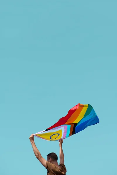 一个穿着棕色T恤的男人的特写 在蓝天的映衬下 在空中挥动着进步骄傲的旗帜 上面有一些空白的地方 — 图库照片