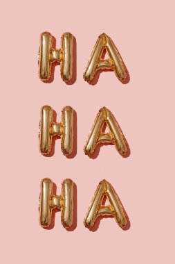 golden letter-shaped balloons forming the interjection ha ha ha, representation of laughter, on a pink background clipart