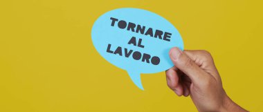 Elinde mavi kağıt levhası olan, sarı arkaplanda, web pankartı olarak kullanılacak panoramik bir formatta, İtalyanca yazılmış işe geri dönen bir adamın eli.