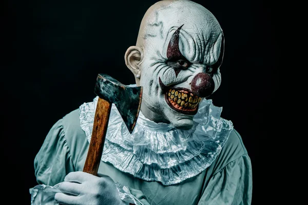 一个毛骨悚然的秃头邪恶小丑的特写镜头 用一把带有血迹的斧头在黑色背景下威胁观察者 — 图库照片