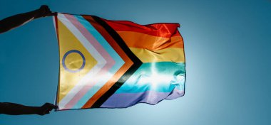 closeup of a man flying an intersex-inclusive progress pride flag on the sky, with the sun in the background, in a panoramic format to use as web banner or header clipart