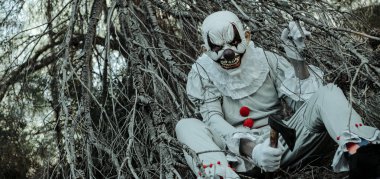 Karanlık çöktüğünde elinde baltayla gri bir kostüm ve kırmızı ponponlar giyen şeytani bir palyaçoya yaklaş. Ağ pankartı ya da başlık olarak kullanmak için panoramik bir formatta ormanın içinde oturuyor.