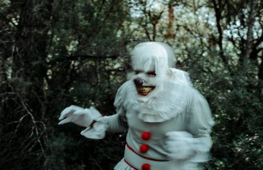 Beyaz fırfırlı ve kırmızı ponponları olan gri kostümlü bulanık, tüyler ürpertici bir palyaço alacakaranlıkta ormanda yürüyordu, korkutucu bir gülümsemeyle.