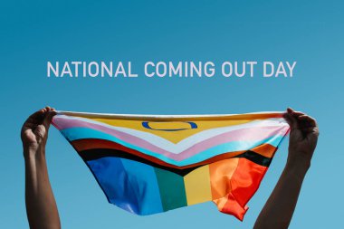 text national coming out day and a young person holding an intersex-inclusive progress pride flag above their head against the blue sky clipart