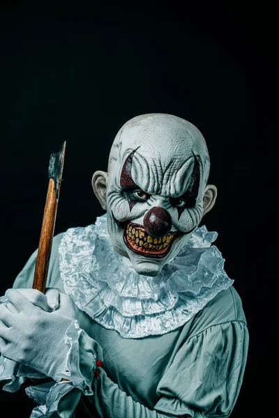 一个毛骨悚然的邪恶小丑 穿着一身白领的灰色服装 举起一把沾满血迹的斧头 在黑色的背景上以可怕的微笑威胁着观察者 — 图库照片