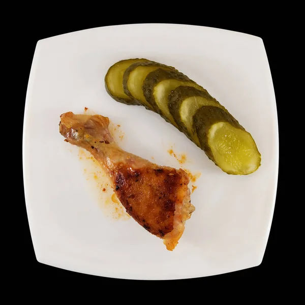 Kızarmış tavuk budu ve beyaz tabakta salatalık turşusu.