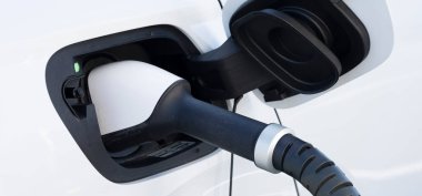 İstasyonda beyaz bir elektrikli araba şarj oluyor.
