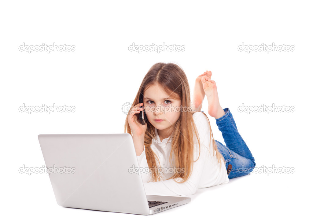 Little girl lying on floor working with a laptop and mobile phon