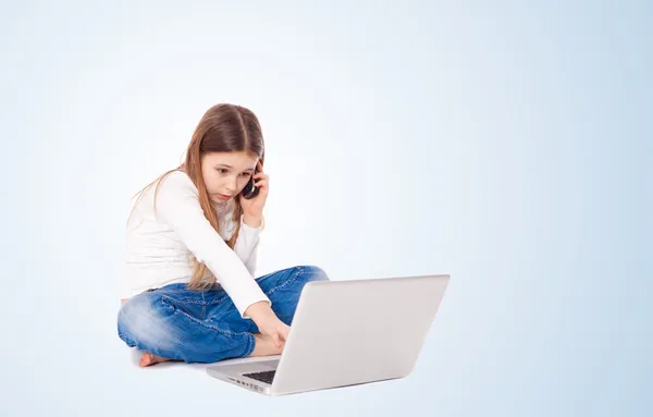 Kleines Mädchen, das am Boden liegt und mit Laptop und Handy arbeitet — Stockfoto