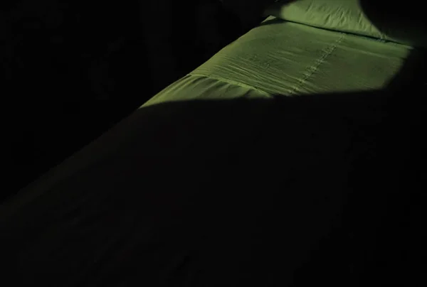 窓から光が差し込む暗い部屋に緑のリネンのベッド — ストック写真