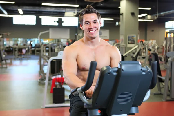 Cheerful young fitness guy working out on exercise bicycle — Stock Photo, Image