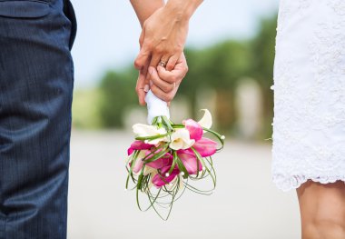 Closeup view of married couple holding hands and carrying bride's bouquet clipart