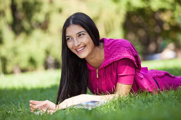 Jong meisje liggen op het gras in het park, lezen van een tijdschrift — Stockfoto