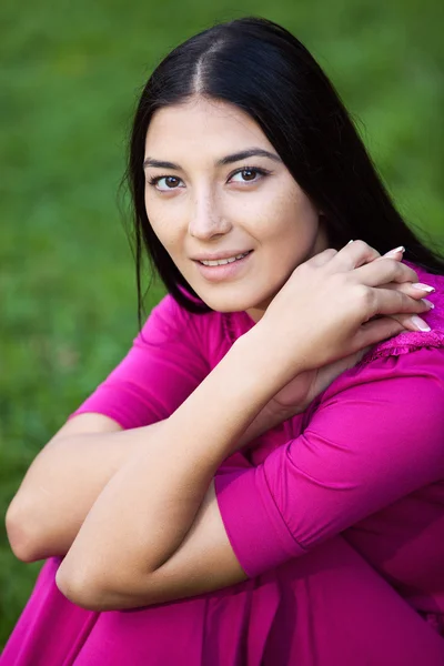 Porträt einer schönen jungen Frau, die auf dem Rasen im Park sitzt — Stockfoto