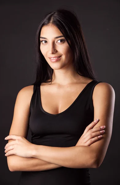 Beautiful young woman standing with her hands folded against black background — Stock Photo, Image