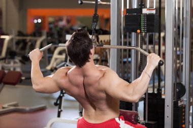 Rear view of young fitness guy working out on exercise machine