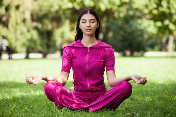 Beautiful young girl meditating while sitting on the grass in a park — Stock Photo, Image