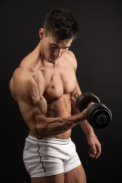 Musculoso joven levantando una mancuerna sobre fondo negro — Foto de Stock
