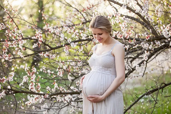 Genç hamile kadın baharda çiçek açan ağaca karşı. — Stok fotoğraf