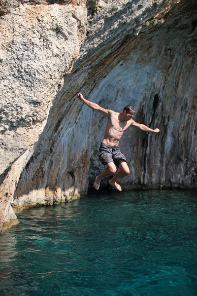 Young man jumping from cliff into sea — Stock Photo, Image