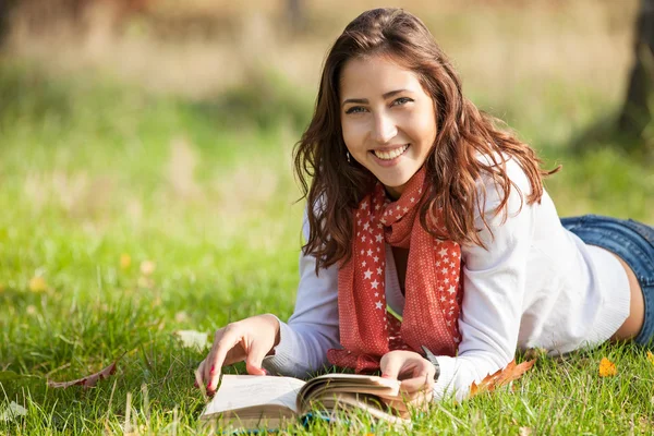 Young girl reading book while lying on grass — Stock Photo, Image