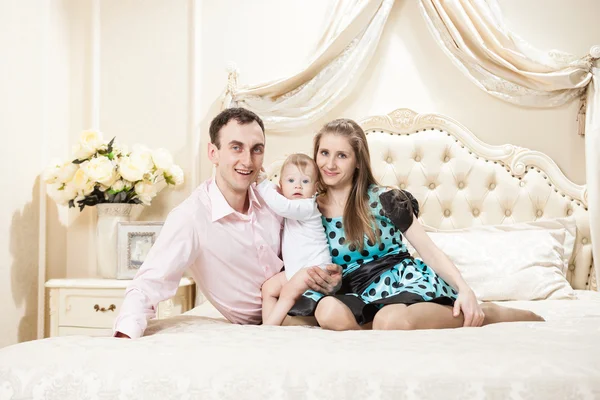 Joven familia feliz con un bebé en la cama — Foto de Stock