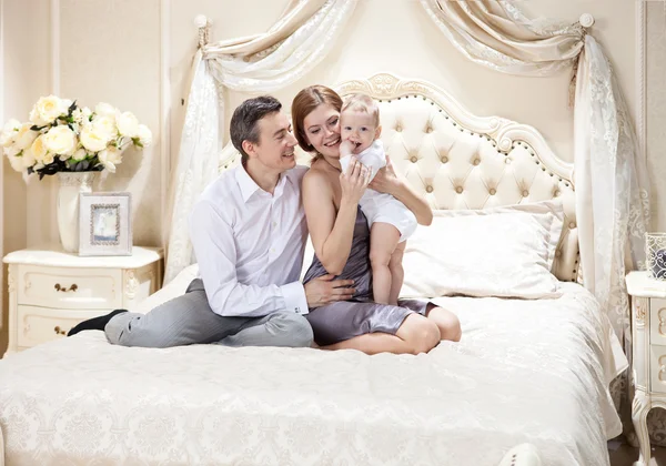 Jonge gelukkige familie met een baby op bed — Stockfoto