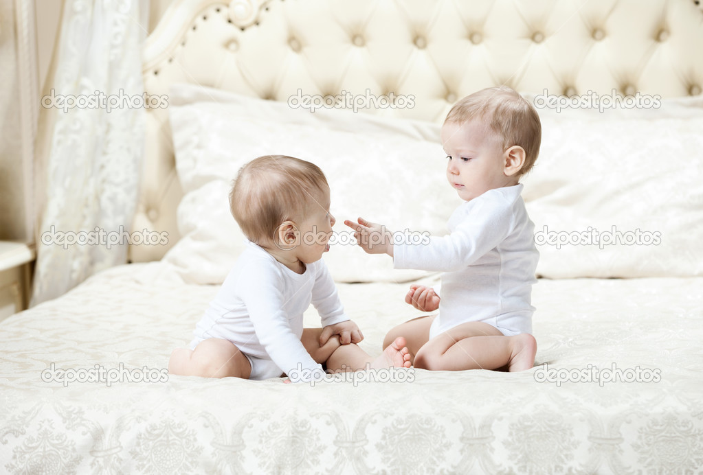 Two baby boys playing on bed