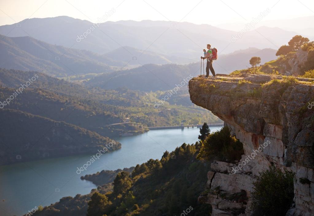 Hiker with baby standing on cliff and enjoying valley view