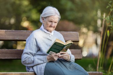Portrait of senior woman on bench in park reading fiction book