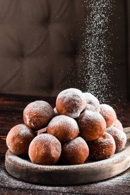 Koyu arkaplandaki ahşap masaya pudra şekeri serpiştirilmiş çörekler Rustik usulü küçük yuvarlak donut topları. Fransız çörekleri.
