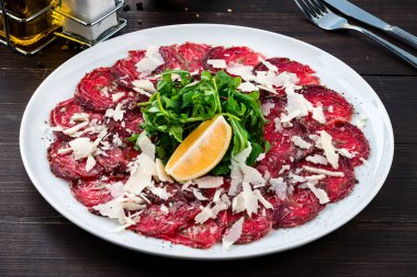 Salata ve limonlu sığır carpaccio, Parmesan peynirli sığır Carpaccio, beyaz tabakta bitki ve vişneli domates.