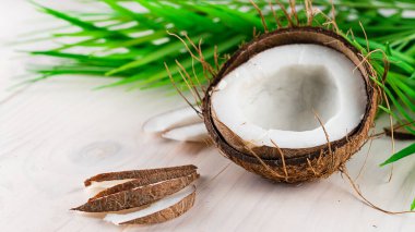 Beyaz ahşap zemin üzerinde hindistan cevizi dilimleri ve palmiye yaprakları, taze hindistan cevizi kompozisyonu ve kopyalama alanı arka planı