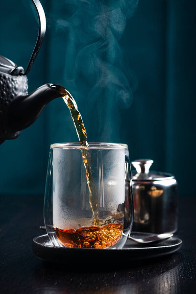 Black tea is poured into a glass cup, hot tea is poured into a glass with steam Pour the hot tea into the teacup