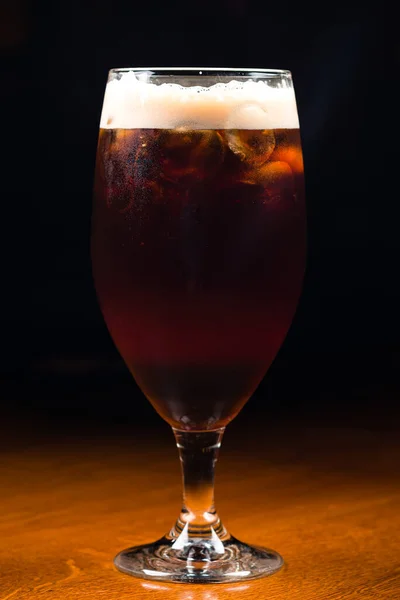 dark beer with ice on the bar counter. Ice cold glass of dark beer with foam. Stout beer freshly poured