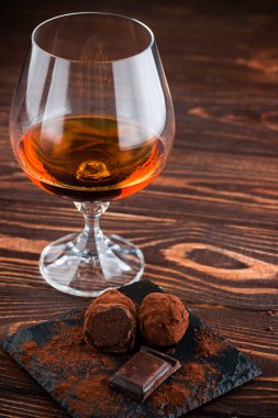 Bir bardak brendi ve çikolatalı trüf mantarı eski ahşap bir masada.