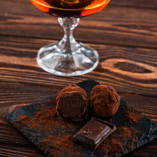 Glass of brandy and a chocolate truffles with chocolate on an old wooden table — 스톡 사진