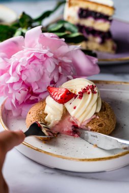 Kadınların elleri pembe çiçeklerin arka planında bir pasta kesiyor.