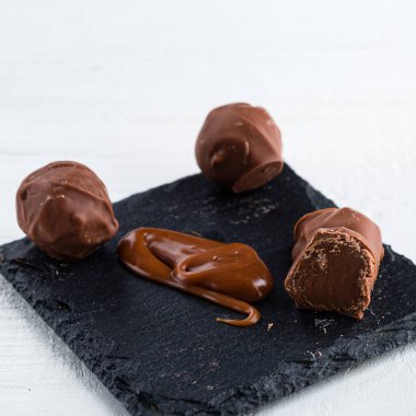 Tuzlu karamelli çikolatalar. Erimiş karamel şekeri ve beyaz arkaplanda tuz bulunan karamel sosu. Gurme tuzlu karamel trüf mantarlarını kapatın.